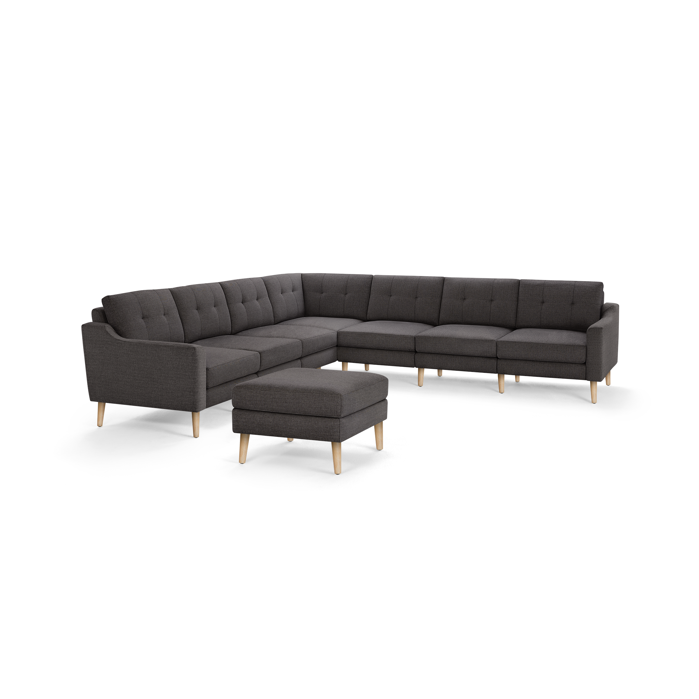 Dark gray L-shaped sectional sofa with tufted back cushions and light wooden legs, accompanied by a matching ottoman.