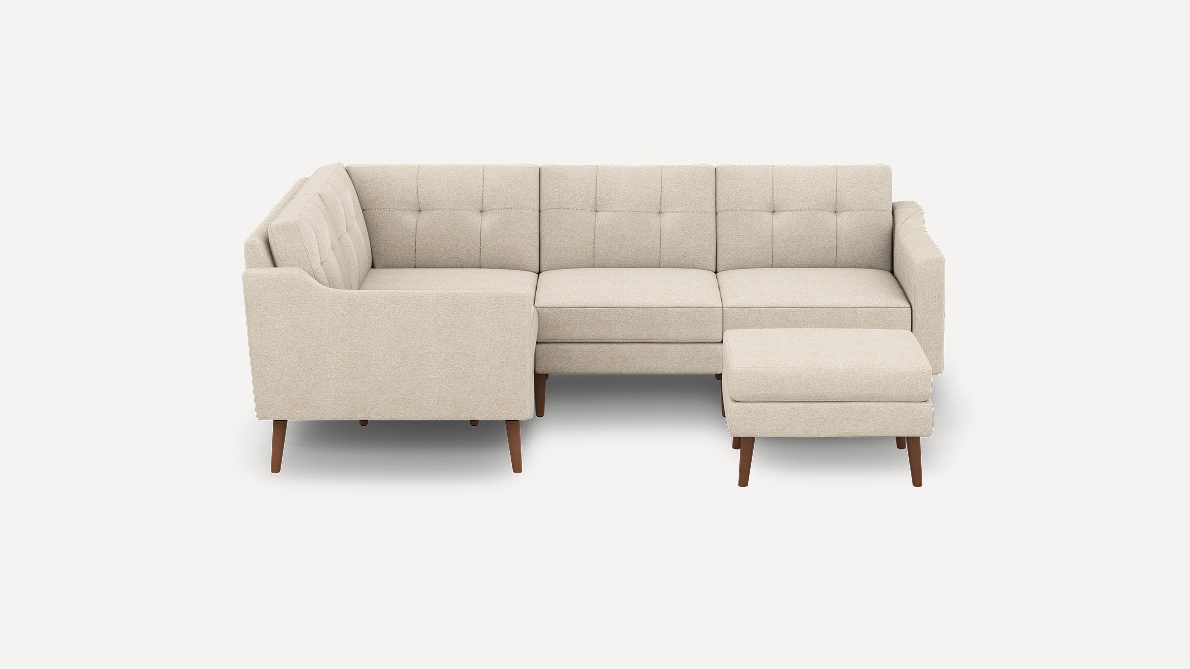 Beige fabric L-shaped sectional sofa with tufted back cushions and matching ottoman, supported by wooden legs.
