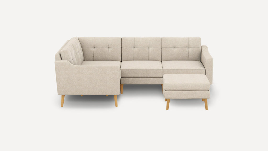 Beige fabric sectional sofa with tufted cushions and matching ottoman, featuring light wooden legs in mid-century modern style.