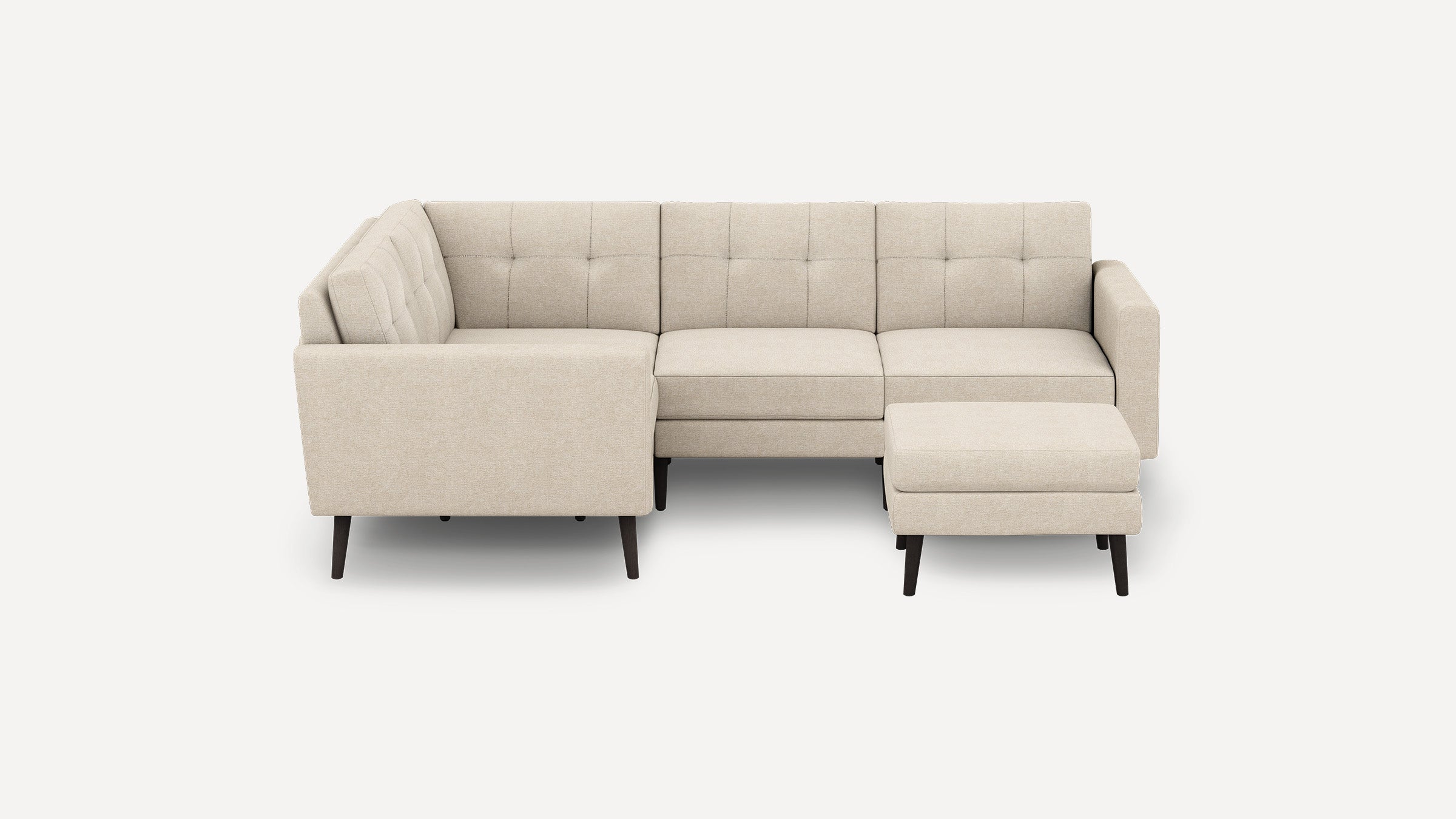 Beige fabric sectional sofa with tufted back cushions and a matching ottoman, supported by dark wooden legs.