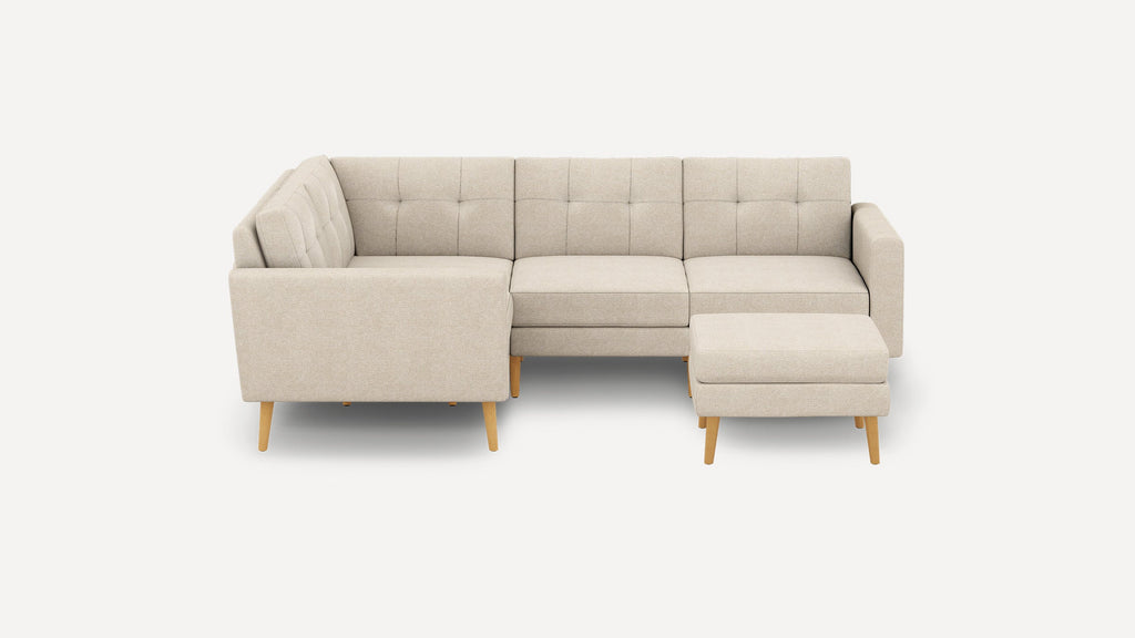Beige L-shaped sectional sofa with tufted cushions and wooden legs, accompanied by a matching ottoman on the right side.