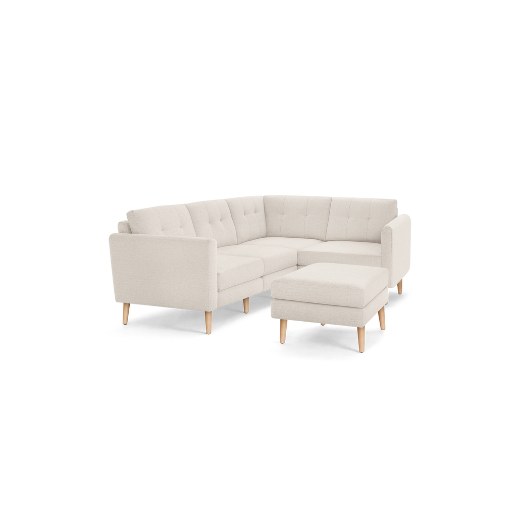 Beige L-shaped sectional sofa with tufted cushions and wooden legs, accompanied by a matching ottoman.