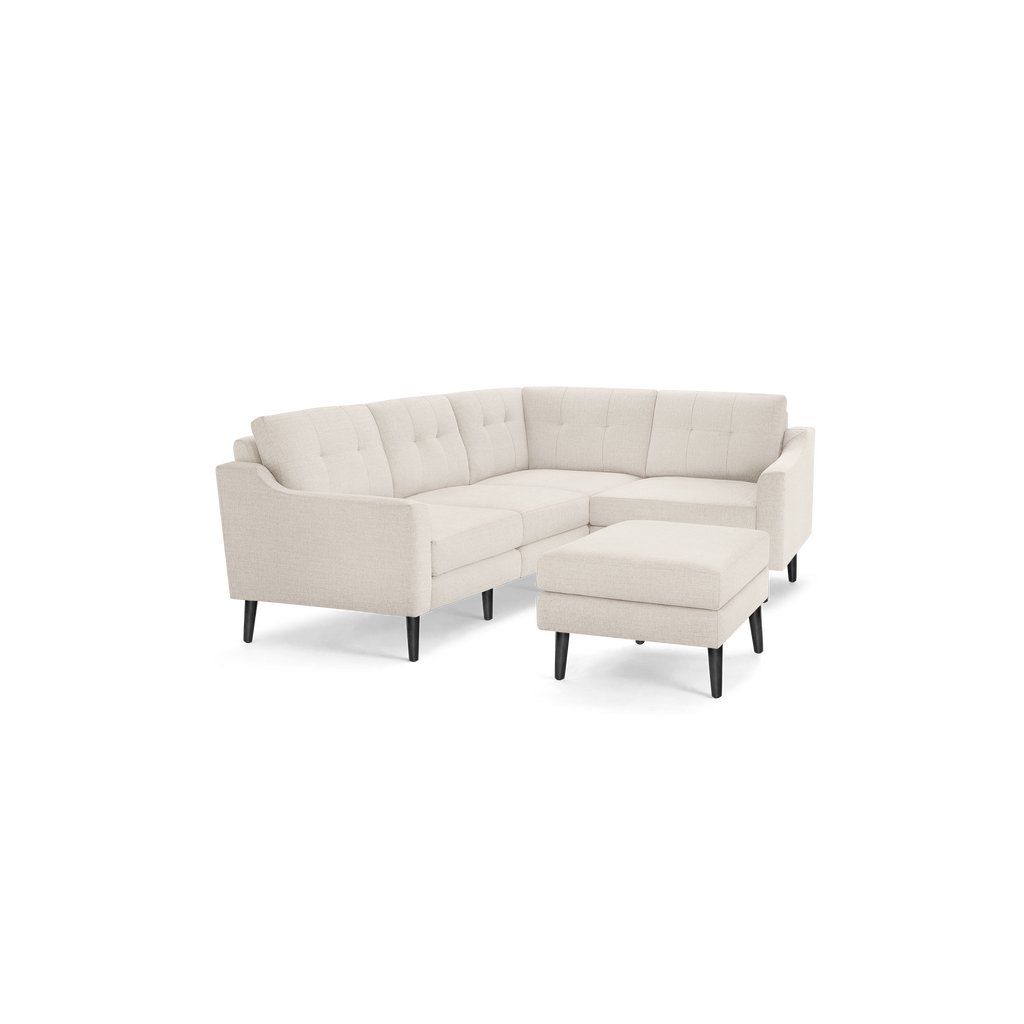 Beige upholstered modern sectional sofa with tufted back cushions, black tapered wooden legs, and matching ottoman.