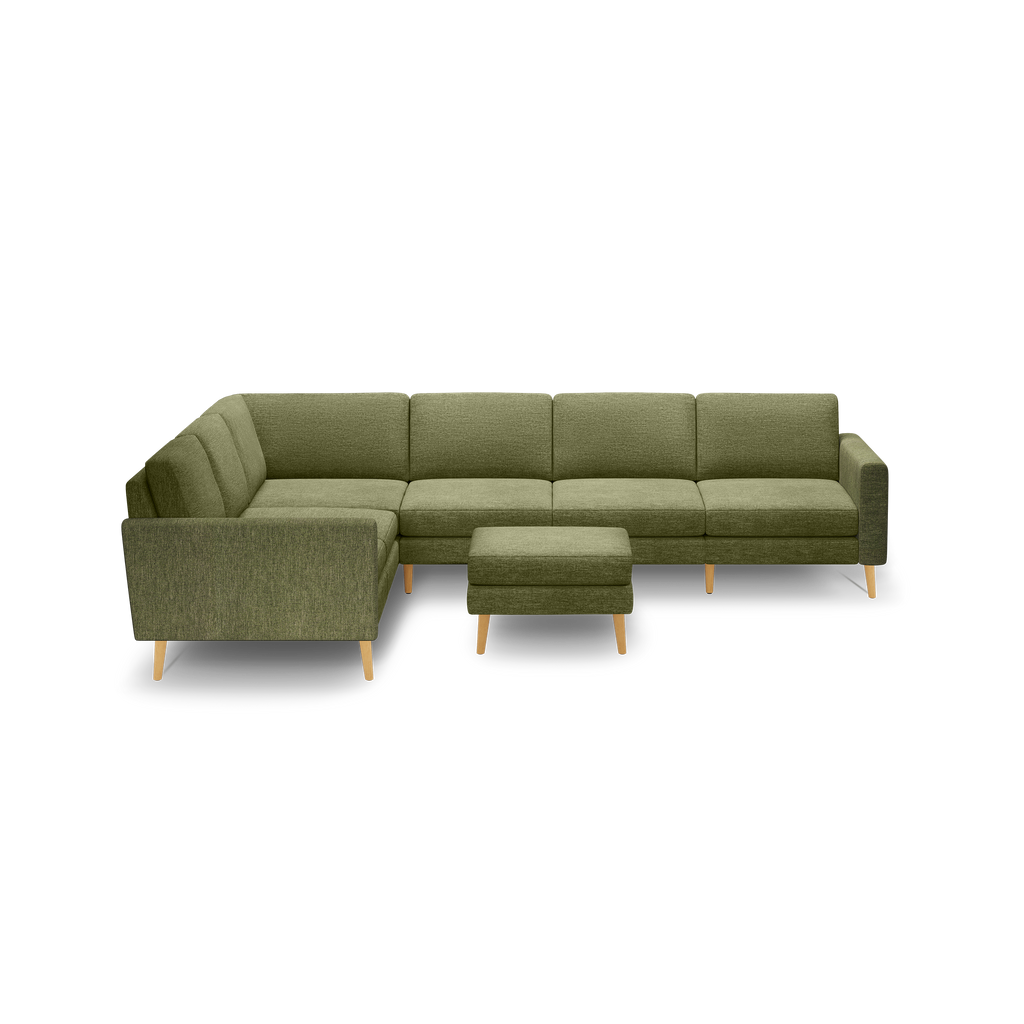 Modern L-shaped sectional sofa in olive green fabric with matching ottoman and light wooden legs, isolated on black background.