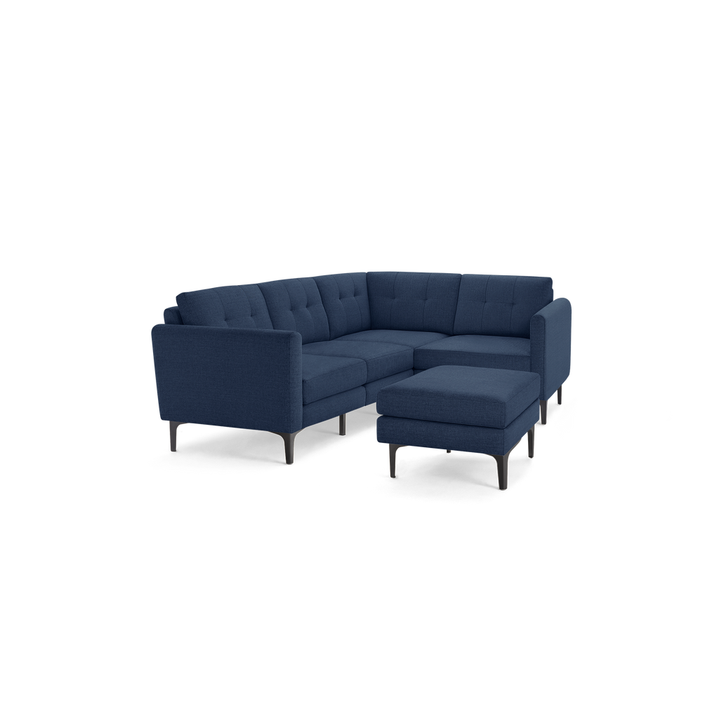 Mid-century modern sectional sofa in navy blue fabric with tufted cushions and black tapered legs, including a matching ottoman.