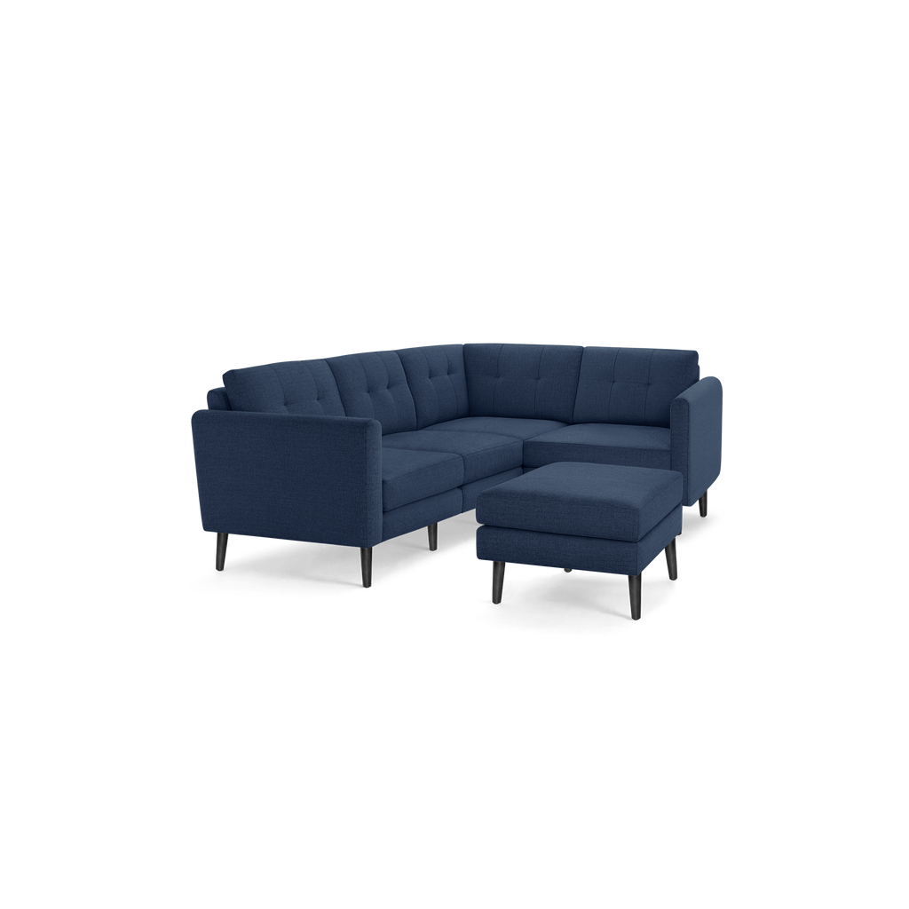 Modern navy blue L-shaped sectional sofa with tufted back cushions and matching ottoman on black wooden legs.