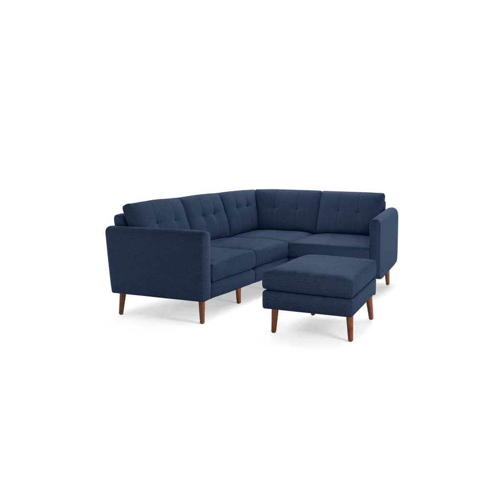 Modern navy blue fabric sectional sofa with tufted back cushions, wooden legs, and a matching ottoman on a black background.