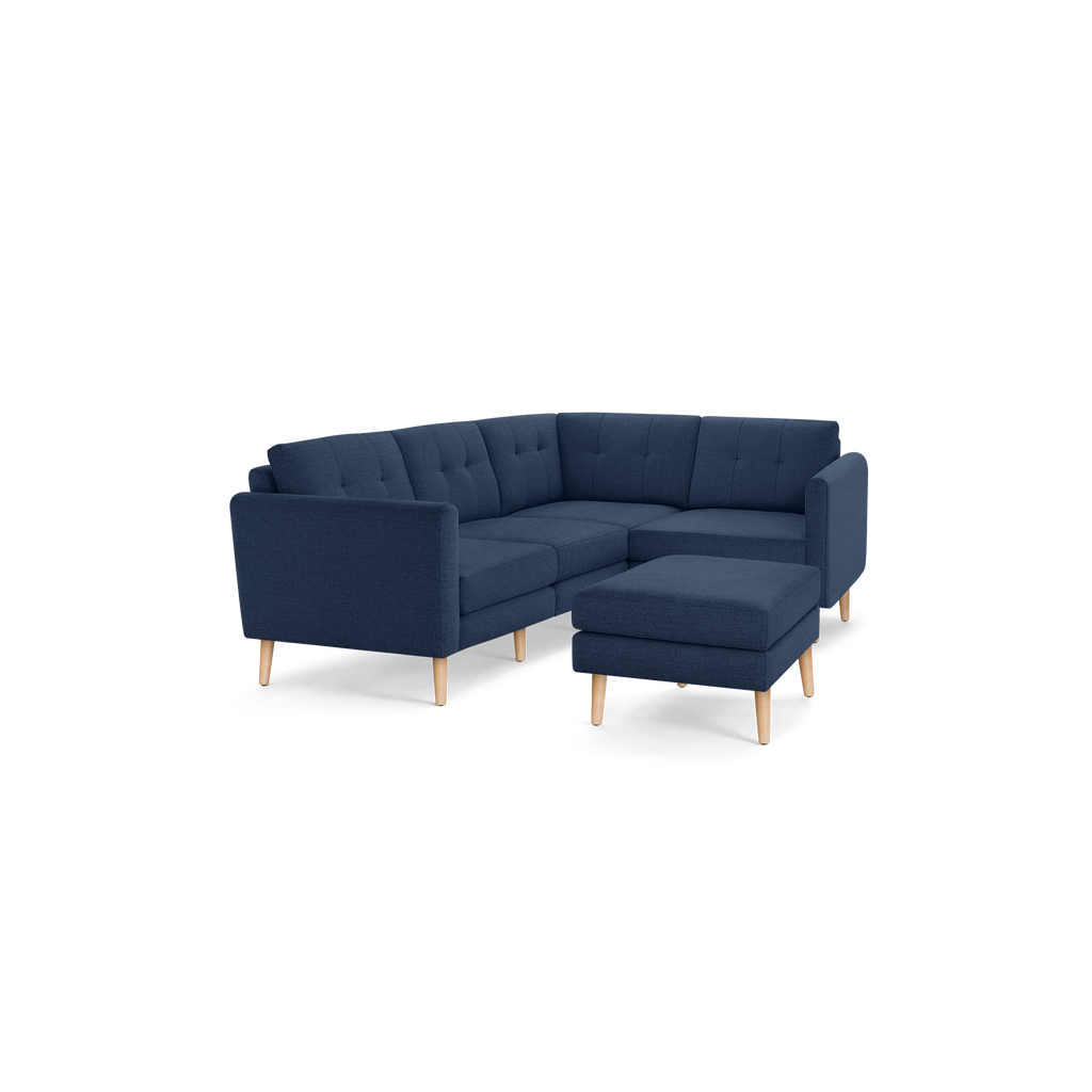 Modern navy blue fabric L-shaped sectional sofa with tufted back cushions and light wooden legs, including a matching ottoman.