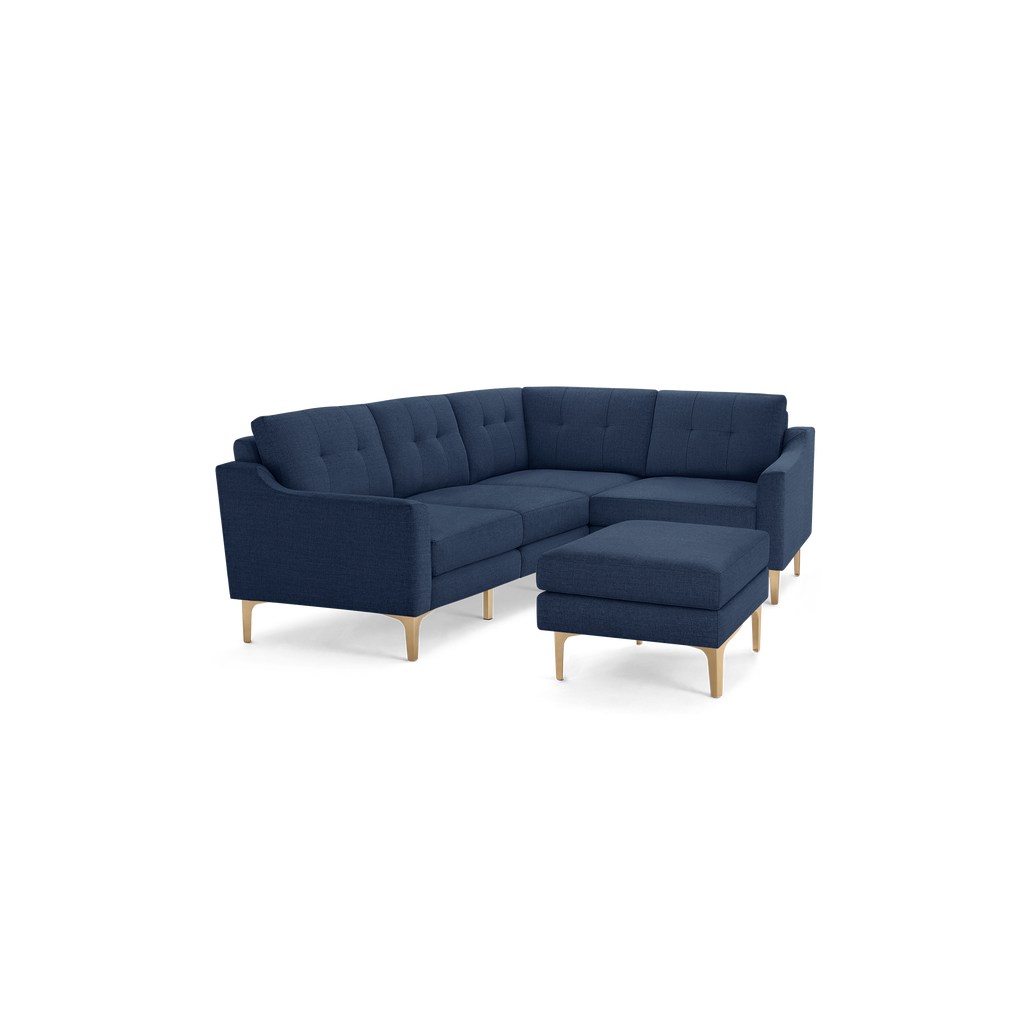Modern navy blue fabric sectional sofa with tufted back cushions and light wood legs, accompanied by a matching ottoman.