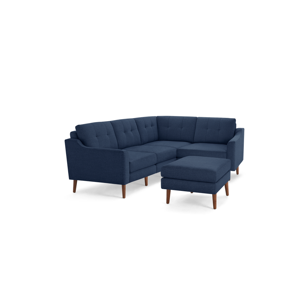 Mid-century modern navy blue fabric L-shaped sectional sofa with tufted cushions and a matching ottoman, supported by wooden legs.
