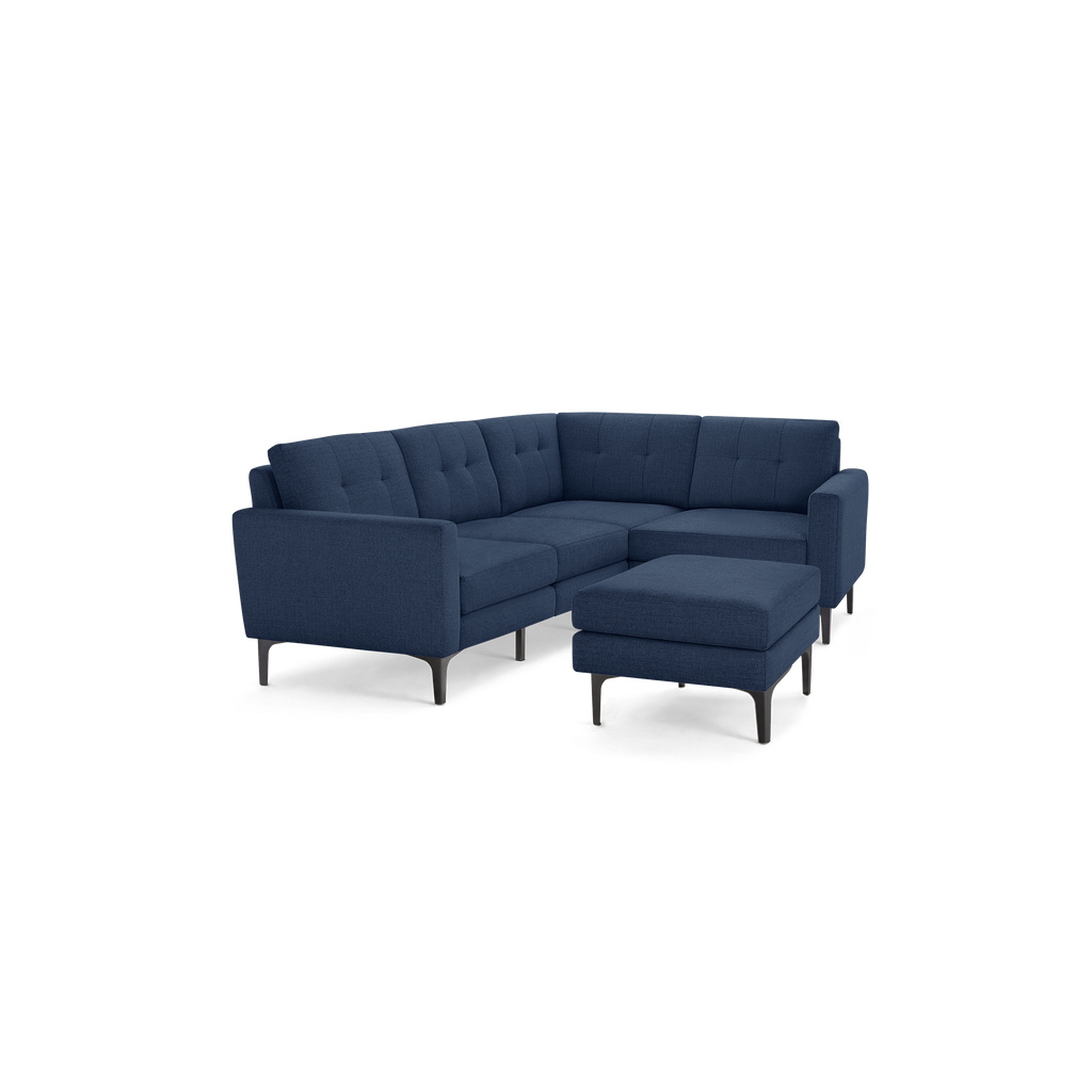 Modern L-shaped sectional sofa in dark blue fabric, featuring tufted cushions and a matching ottoman with slim black legs.