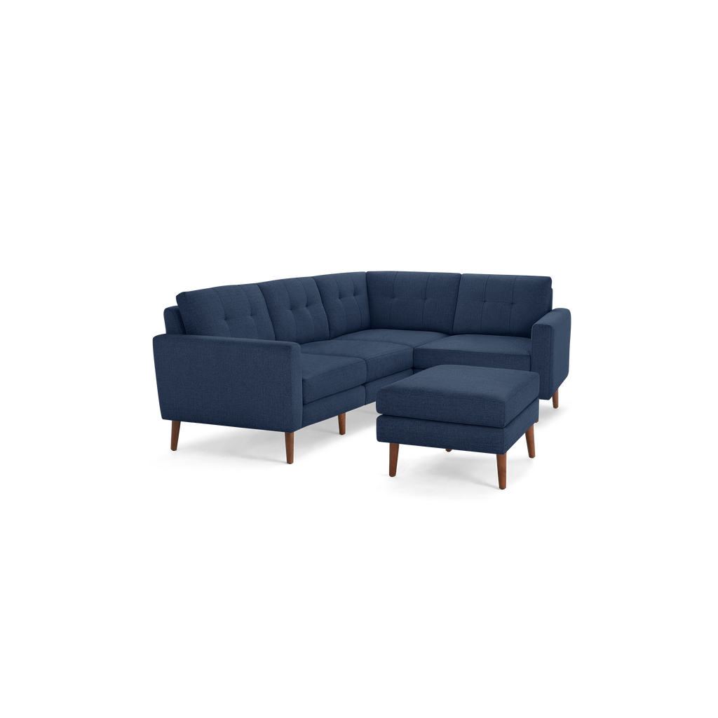 Modern navy blue fabric L-shaped sectional sofa with tufted backrest and matching ottoman, supported by wooden legs.