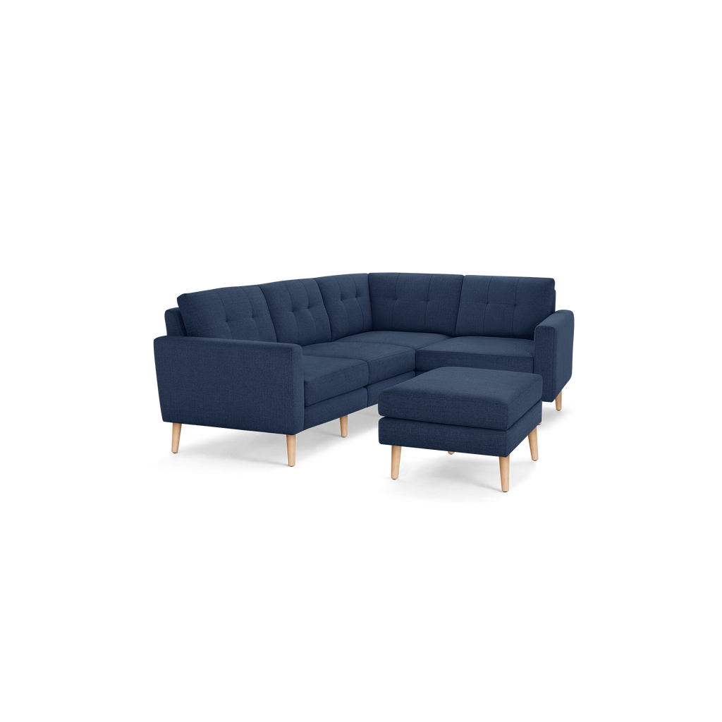 Modern navy blue fabric sectional sofa with tufted cushions, wooden legs, and matching ottoman isolated on black background.