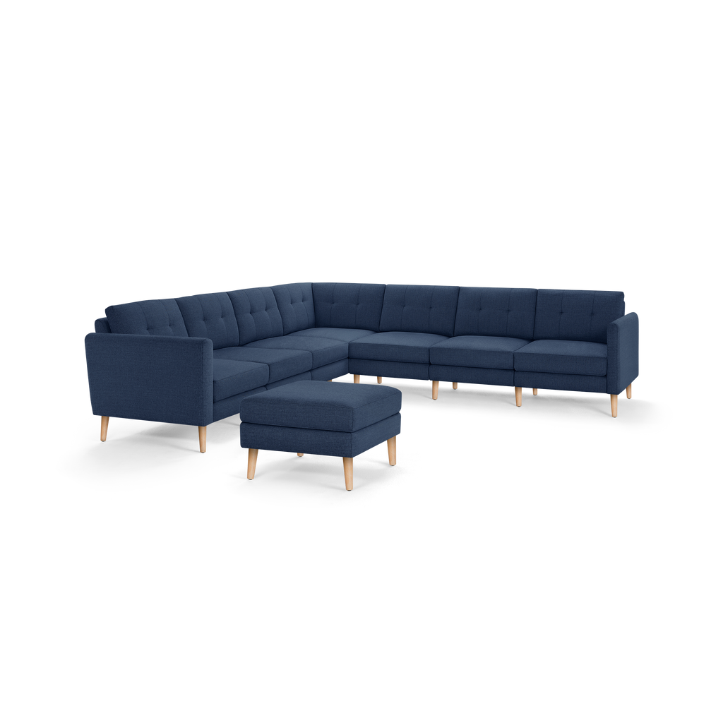 Large navy blue L-shaped sectional sofa with button-tufted back cushions and light wooden legs, accompanied by a matching ottoman.
