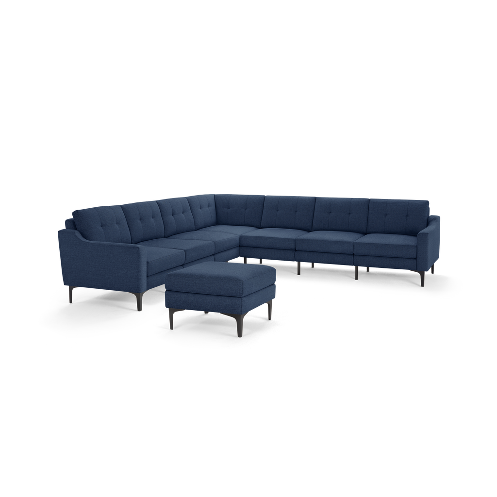 Modern L-shaped sectional sofa in dark blue fabric with tufted back cushions and matching ottoman, supported by slim black legs.