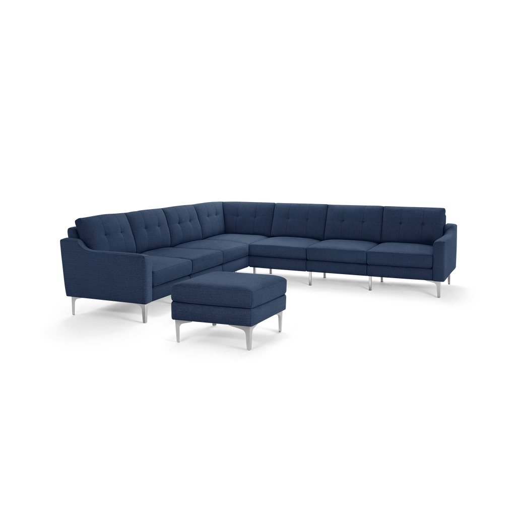 Modern large L-shaped sectional sofa in dark blue fabric with tufted back cushions and matching ottoman on silver metal legs.