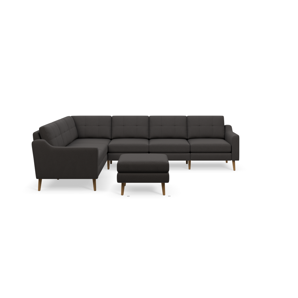 Dark gray fabric L-shaped sectional sofa with tufted cushions, wooden legs, and matching ottoman against black background.