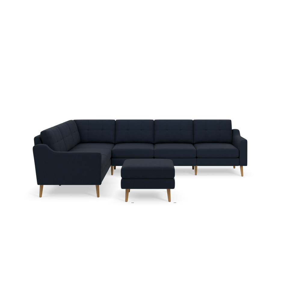 Dark blue sectional sofa with tufted cushions, wooden legs, and matching ottoman on black background.