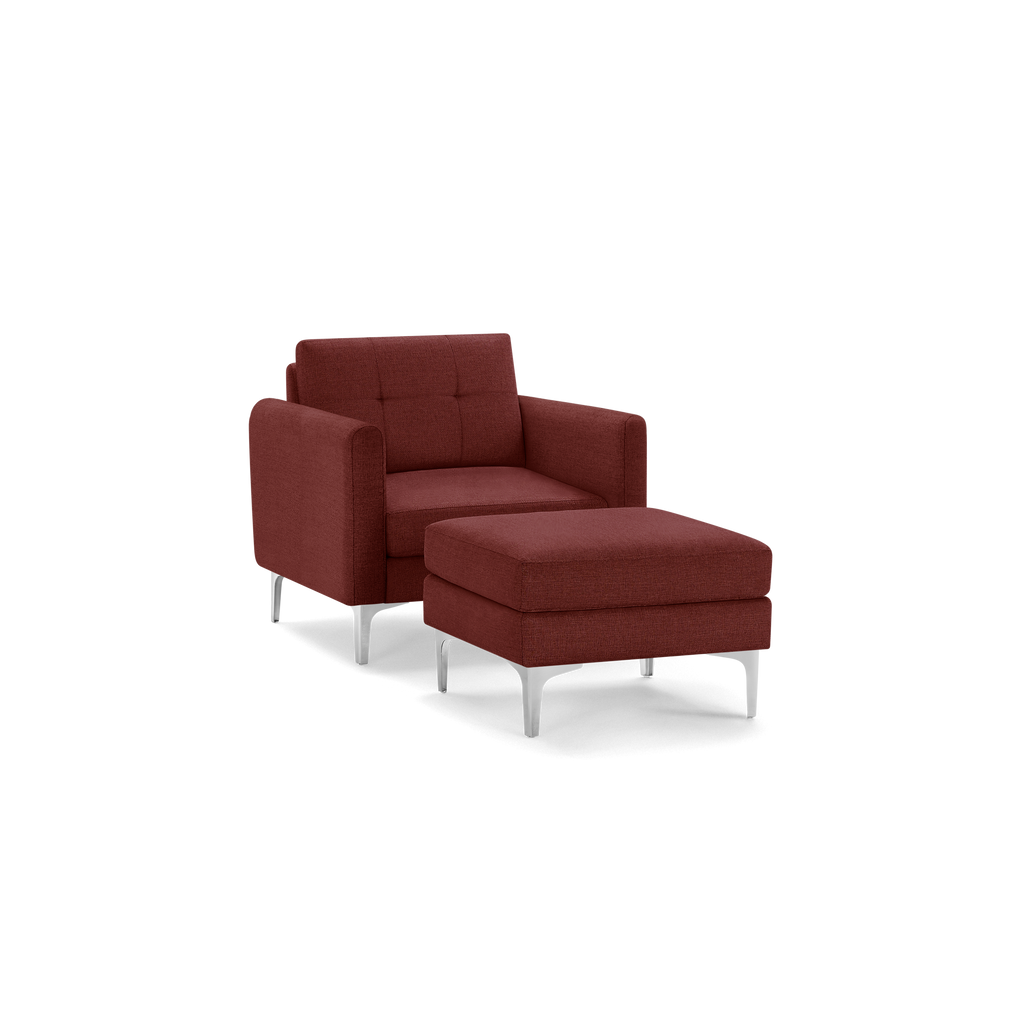 Modern maroon fabric armchair with matching cushioned ottoman and sleek silver metal legs on a black background.