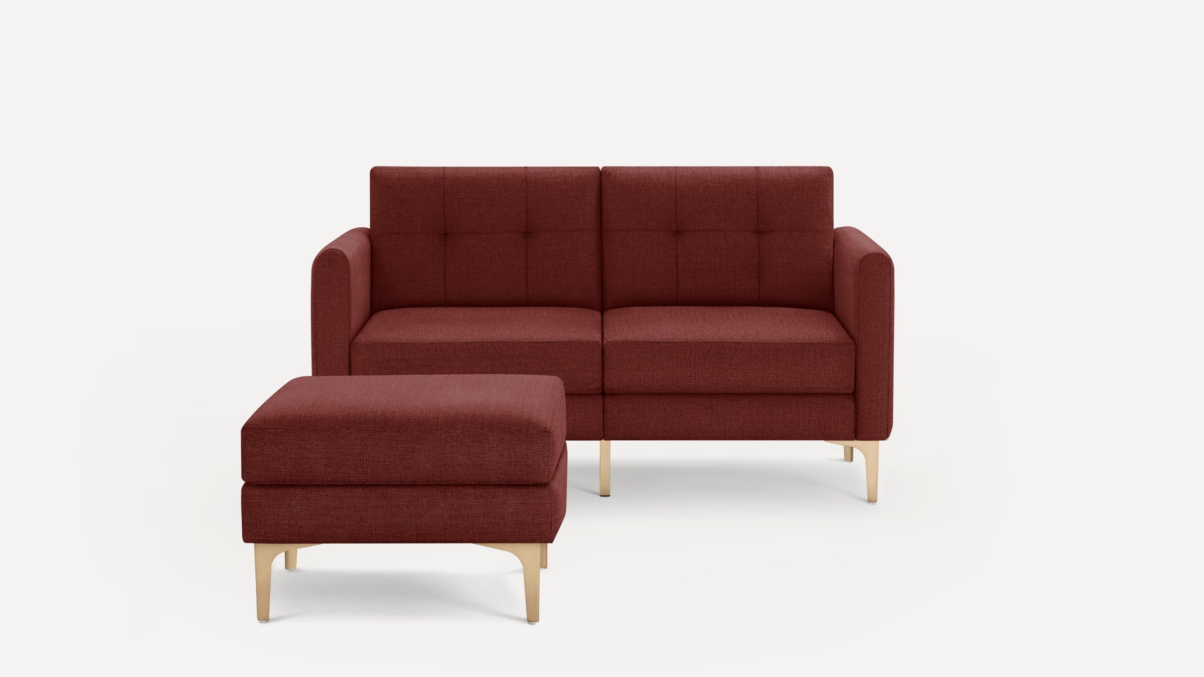 Modern two-seater sofa and matching ottoman in deep red fabric with tufted cushions and light wood legs, minimalist design.