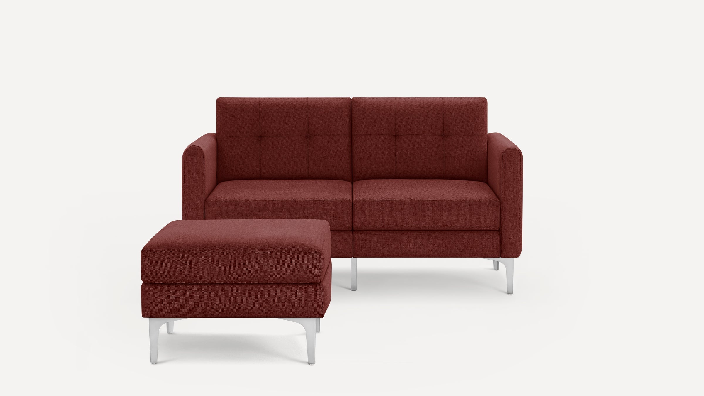 Modern two-seater sofa and matching ottoman in deep red fabric with tufted backrest and sleek silver metal legs.