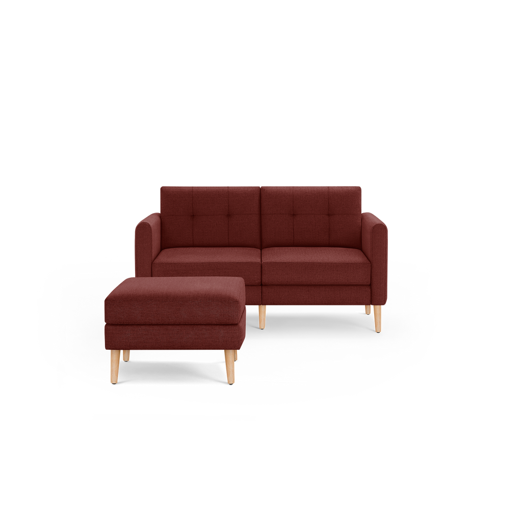 Compact modern two-seat sofa with matching ottoman, upholstered in deep red fabric with light wooden legs.