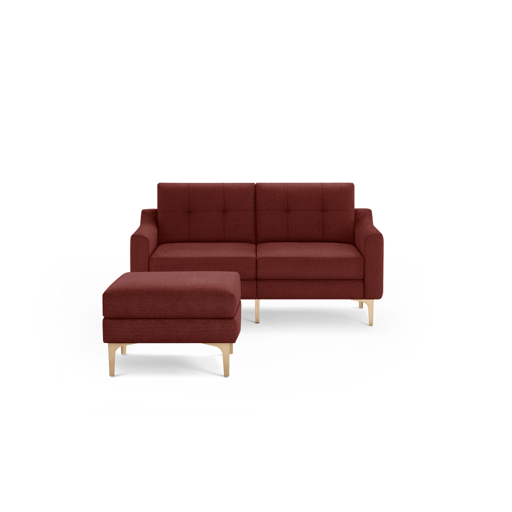 Modern two-seater sofa and matching ottoman in deep red fabric with tufted cushions and light wooden legs, isolated on black background.