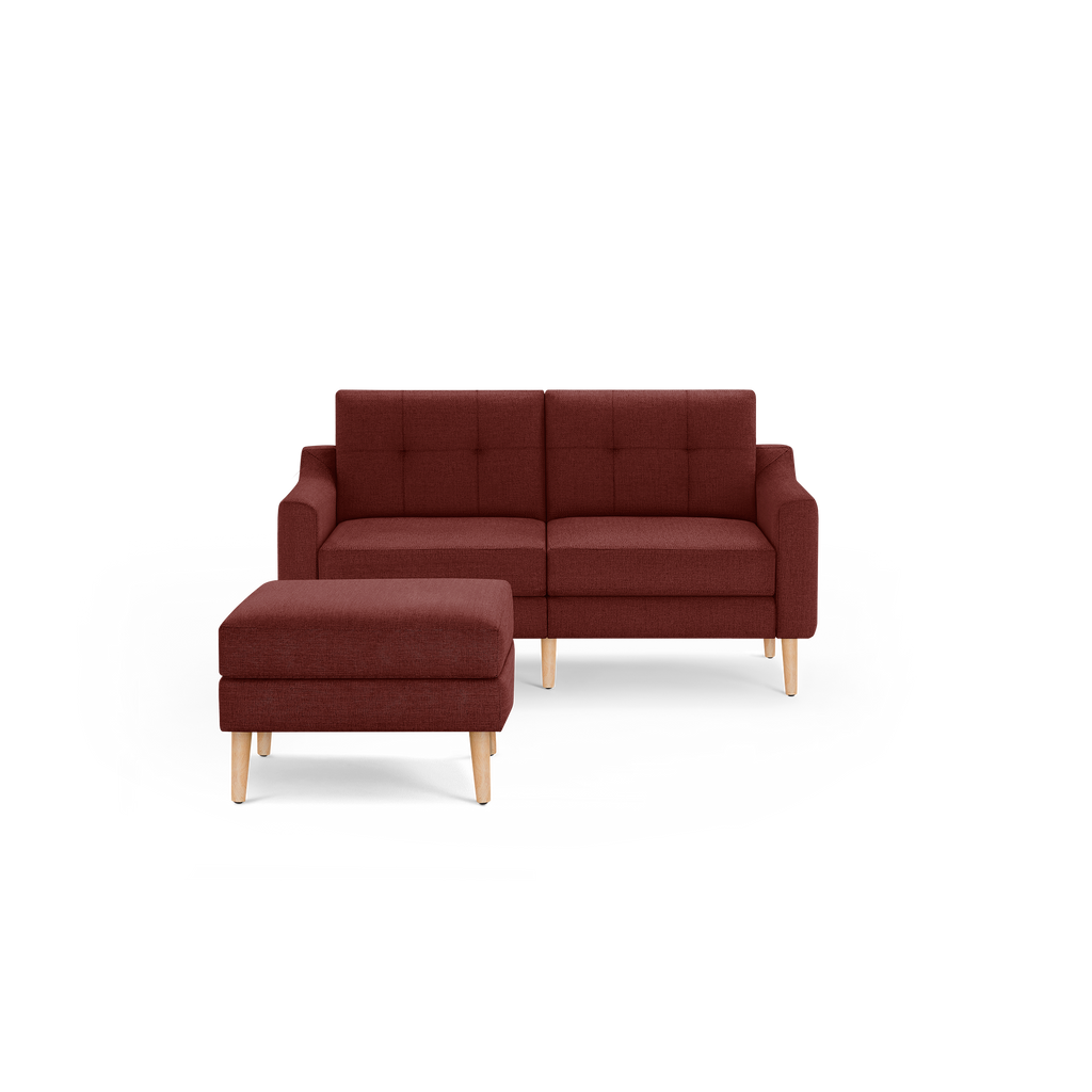 Modern mid-century style two-seater sofa and ottoman in deep burgundy fabric with light wooden legs and tufted backrest cushions.