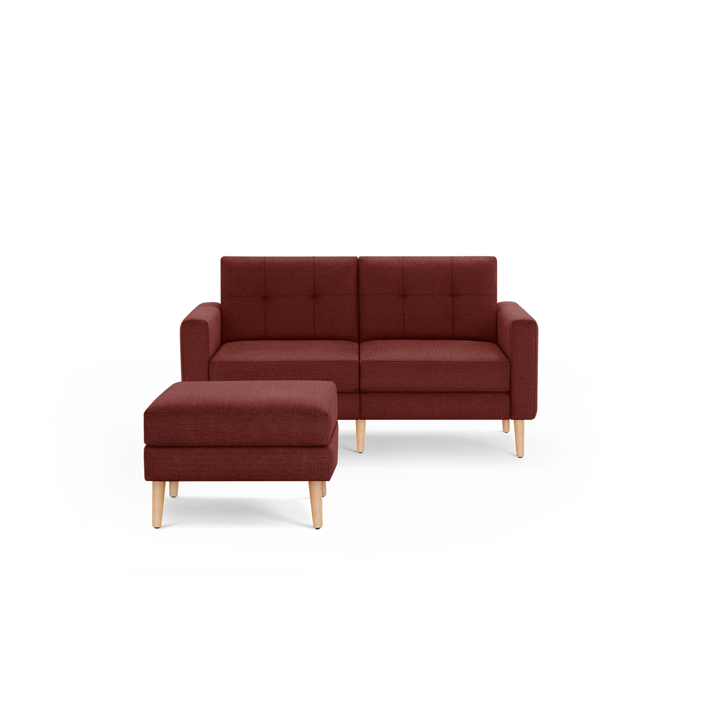 Compact two-seater sofa with matching ottoman, upholstered in deep brown fabric with tufted backrest and light wooden legs.