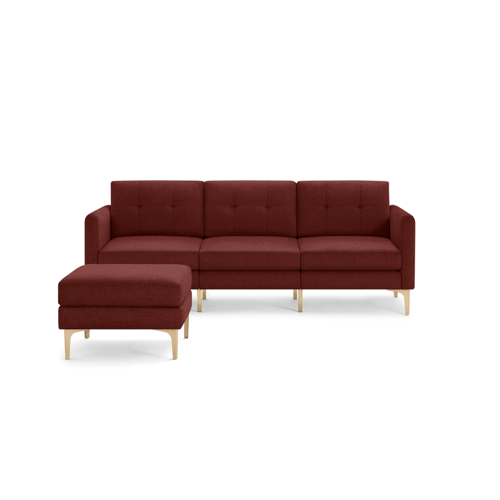 Modern sectional sofa with deep red upholstery, tufted back cushions, and light wooden legs, featuring a matching ottoman.