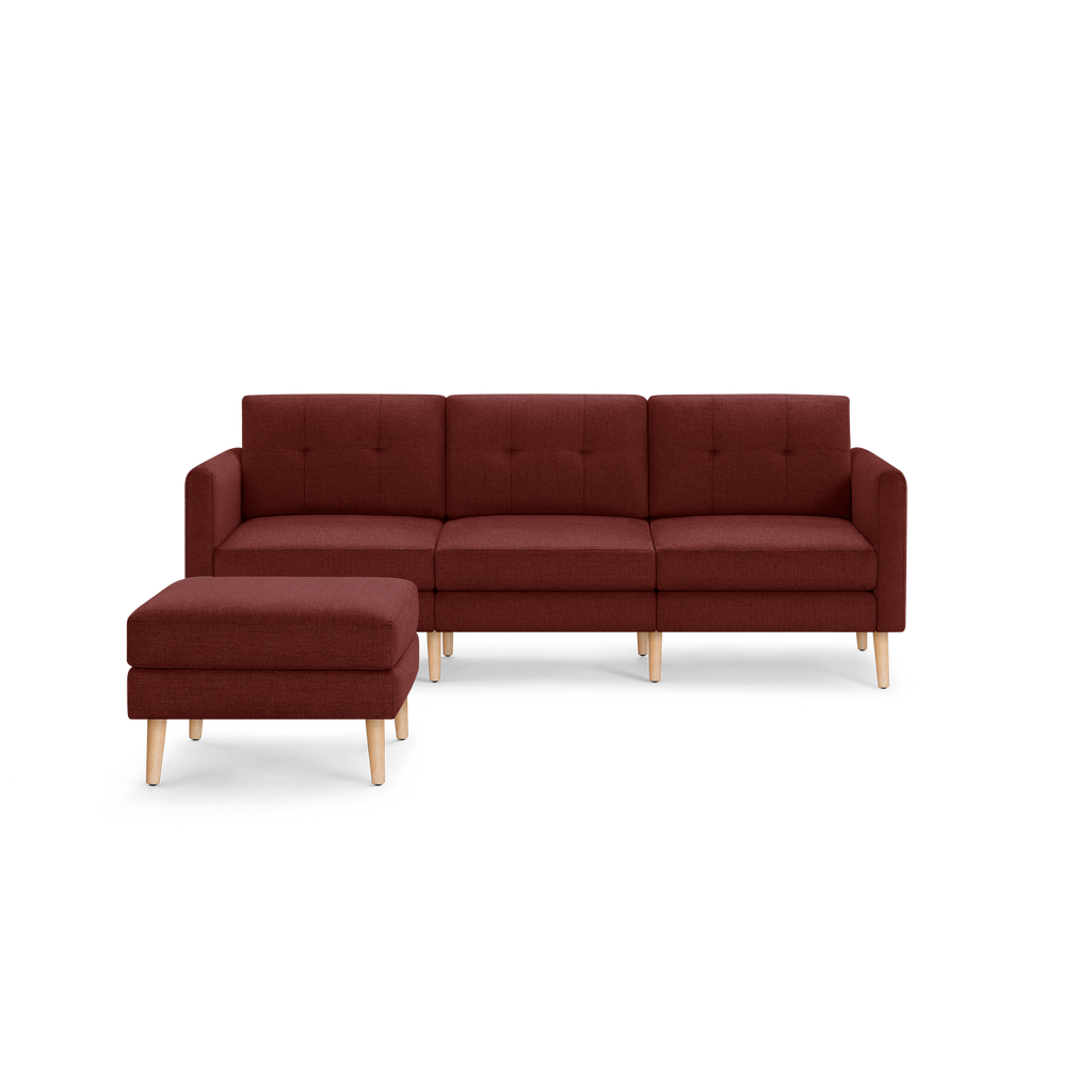 Modern three-seater sectional sofa with matching ottoman in deep red fabric, featuring tufted cushions and light wooden legs.