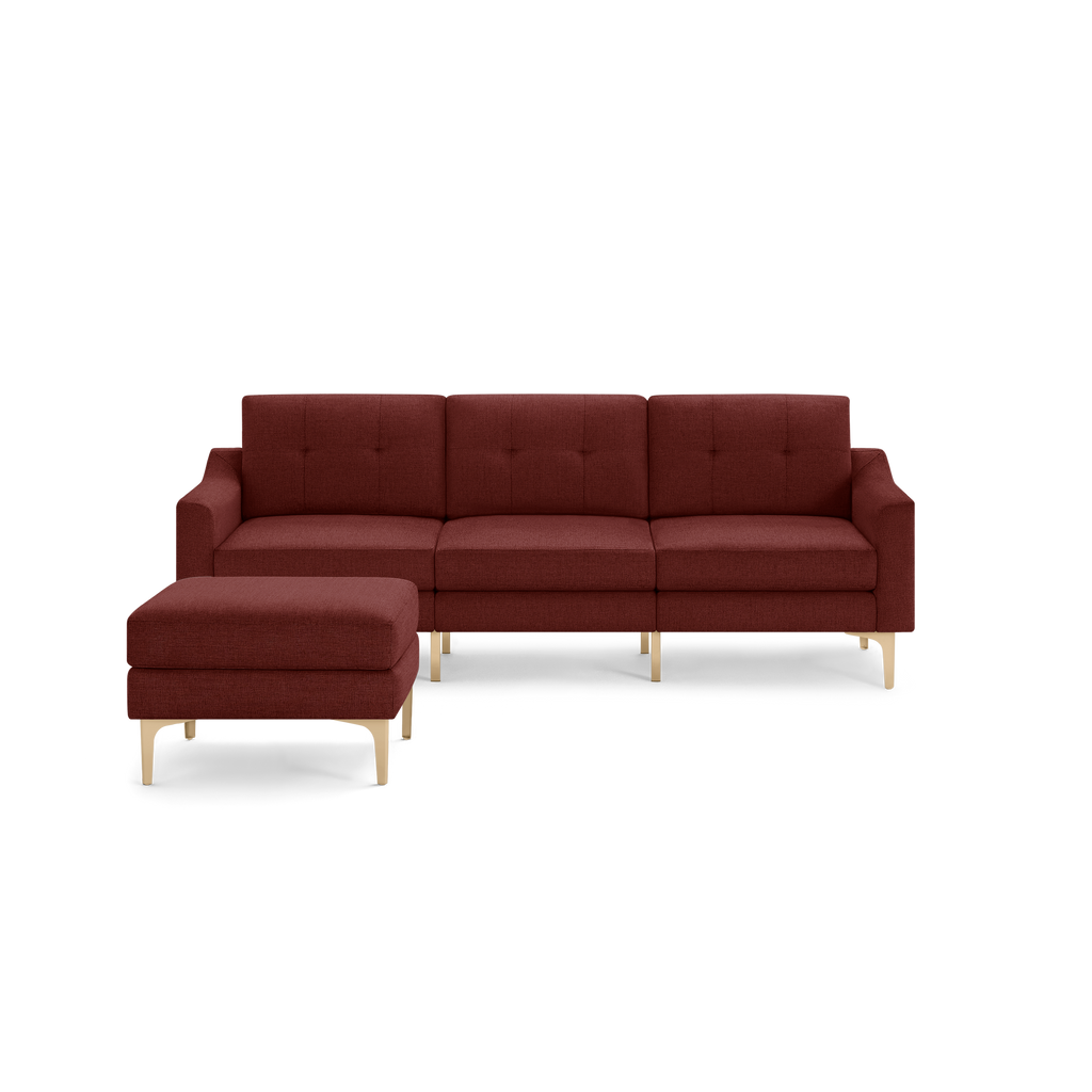 Modern sectional sofa in deep red fabric with button tufting and light wooden legs, including a matching ottoman.