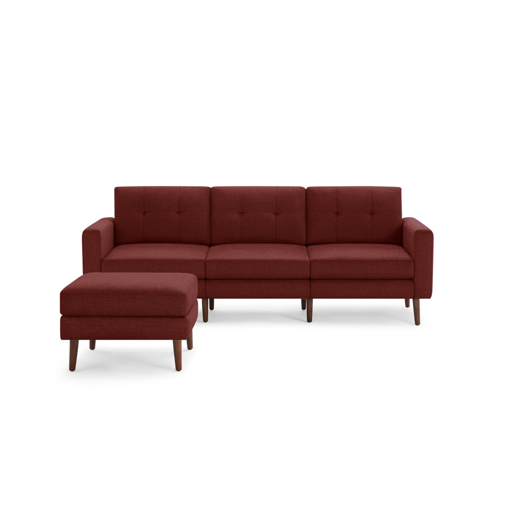 Modern three-seater sofa with tufted cushions and matching ottoman in deep red fabric and wooden legs.