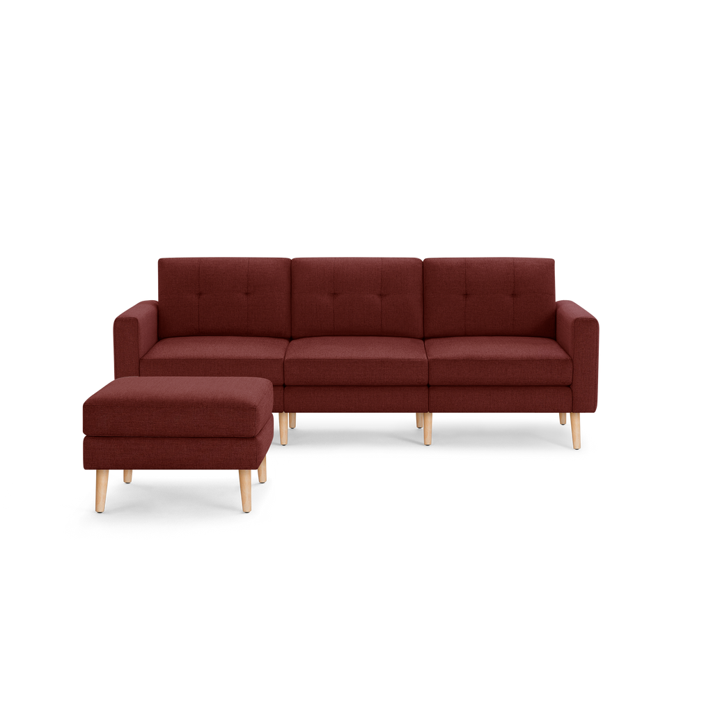 Modern three-seater burgundy fabric sofa with tufted back cushions and matching ottoman, featuring light wooden tapered legs.