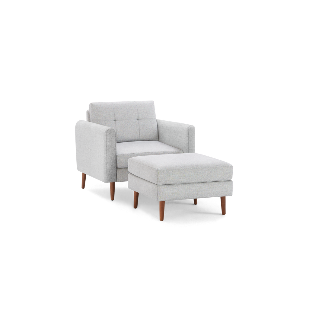 Light gray fabric armchair with tufted backrest and matching ottoman, both featuring wooden legs in mid-century modern style.