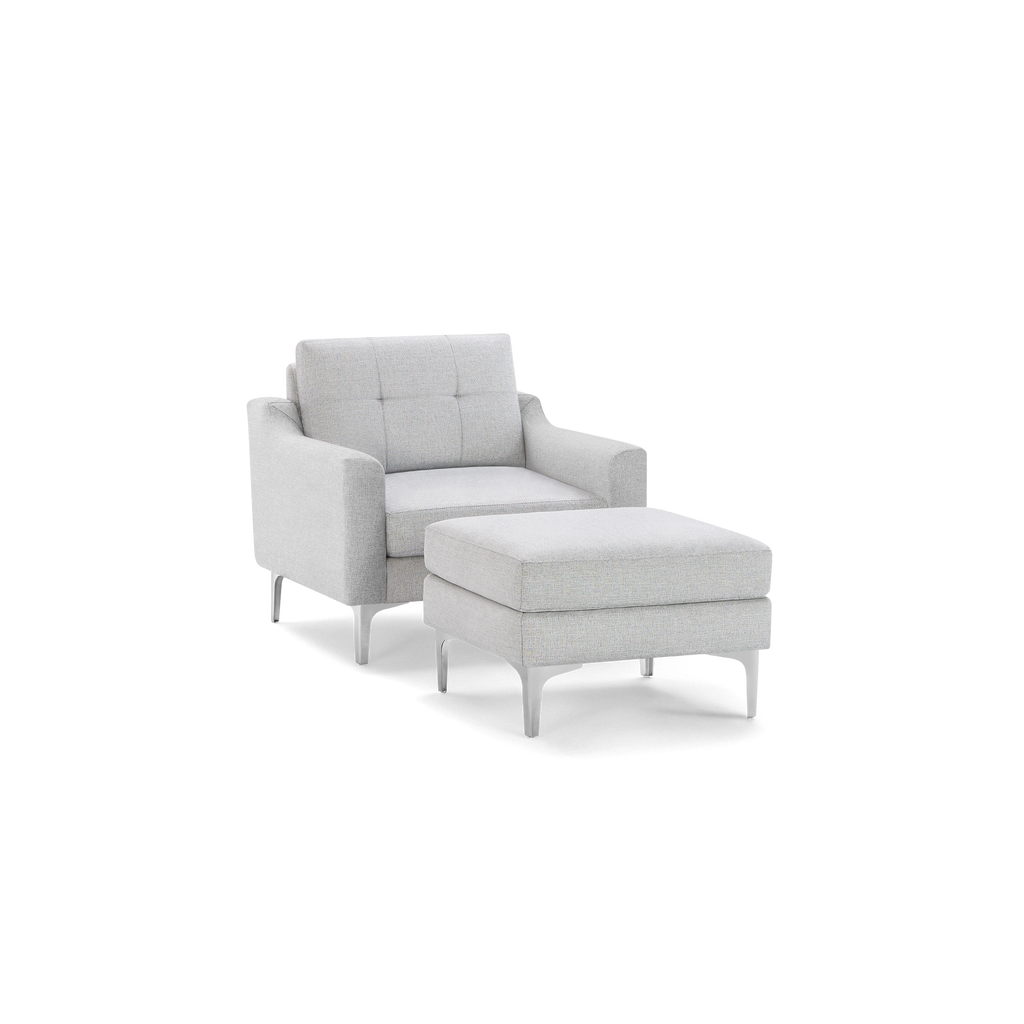 Light gray upholstered armchair with tufted backrest and matching cushioned ottoman, both featuring sleek silver legs.