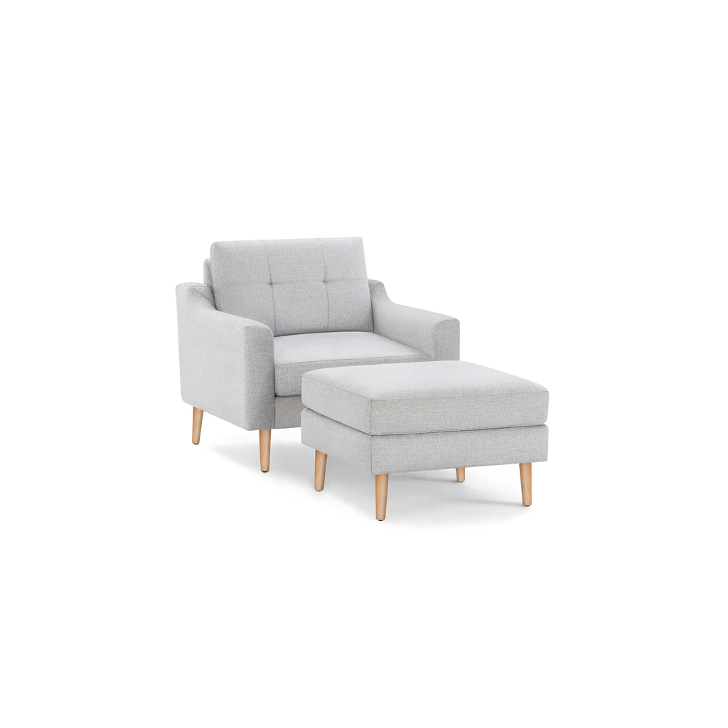Modern light gray fabric armchair with tufted backrest and matching ottoman, both featuring natural wooden legs.