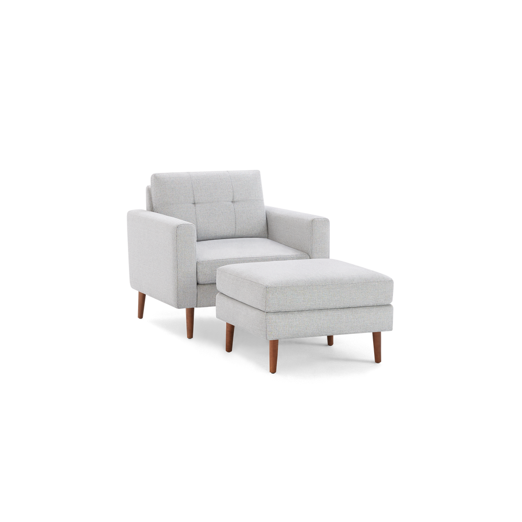 Light gray upholstered armchair with button-tufted backrest and matching ottoman, both featuring wooden legs.