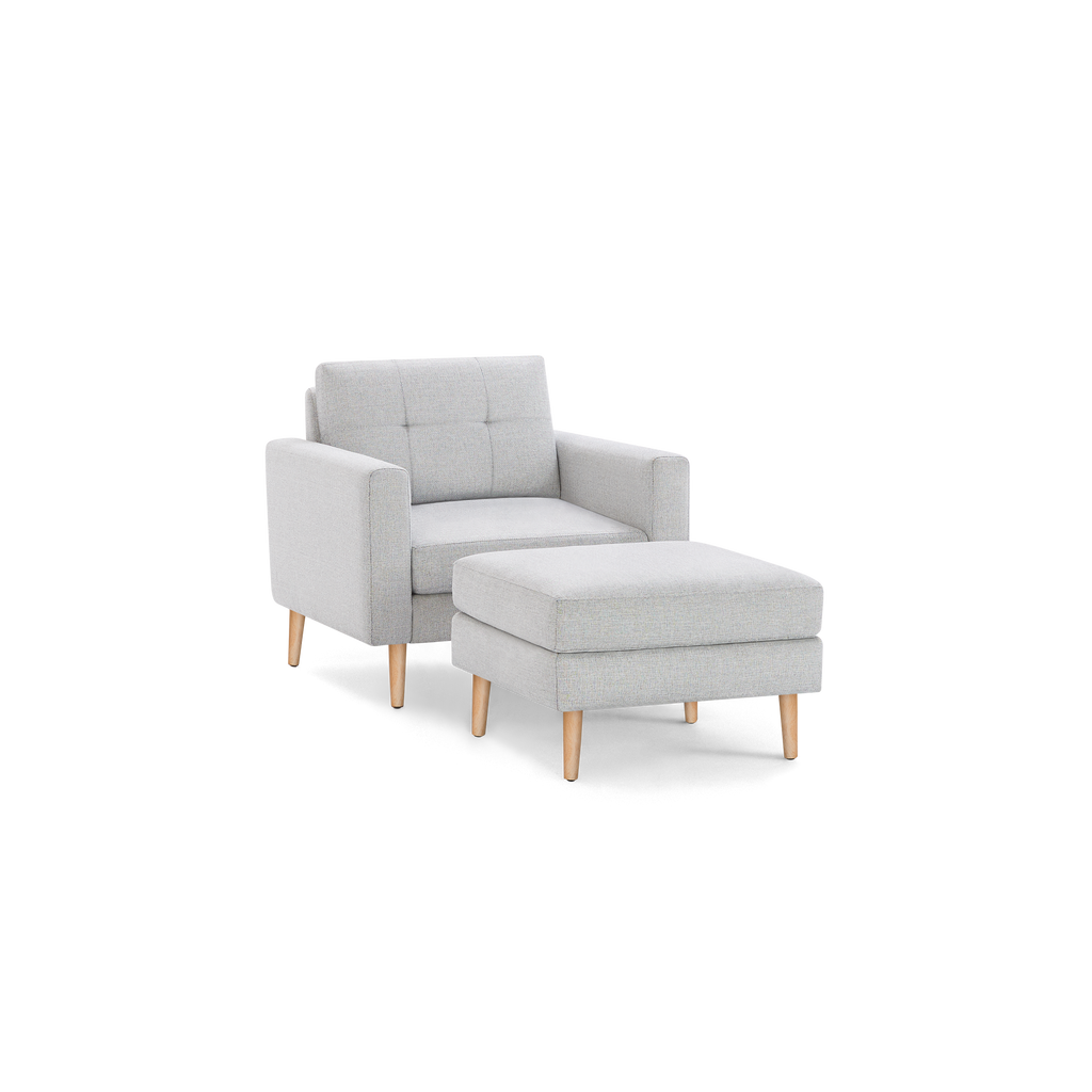 Light gray fabric armchair with matching cushioned ottoman, both featuring light wooden legs and a modern, minimalist design.