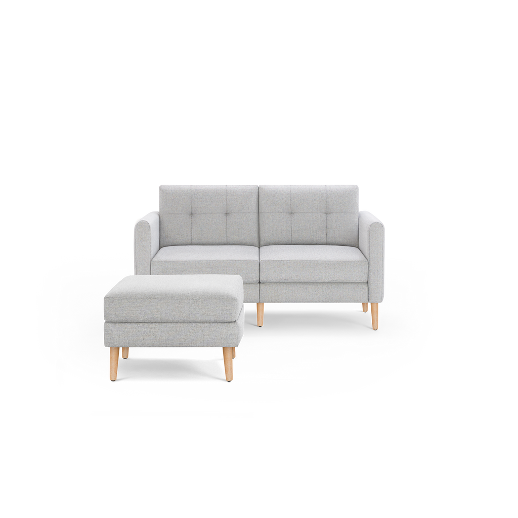 Light gray two-seater sofa with a matching ottoman, both featuring wooden legs and tufted cushion detailing.