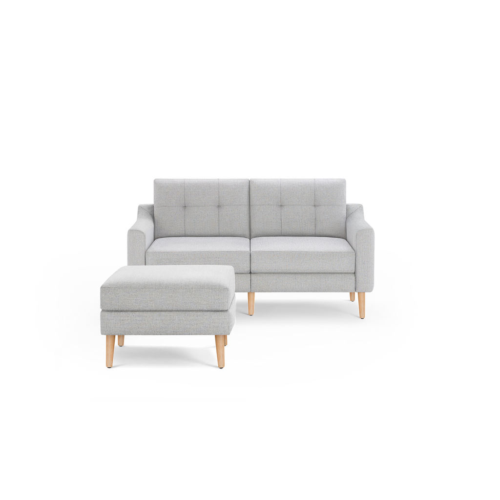 Light gray fabric loveseat sofa with wooden legs, tufted backrest, and matching ottoman against a black background.