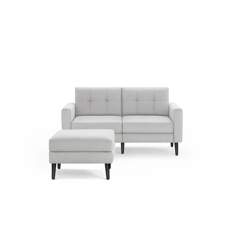 Light gray upholstered two-seat sofa with tufted backrest and matching ottoman, featuring black wooden legs.