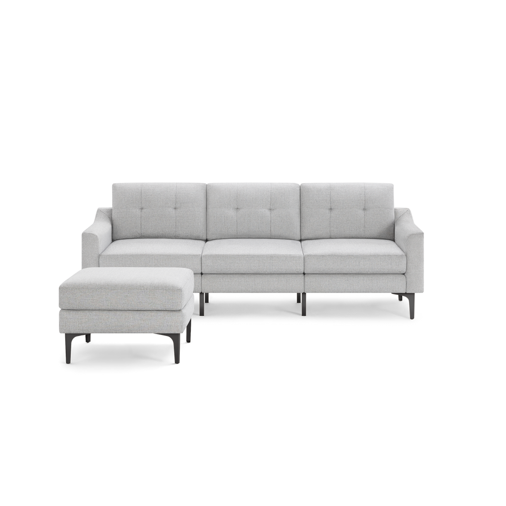 Light gray fabric sectional sofa with tufted back cushions and matching ottoman on black metal legs.