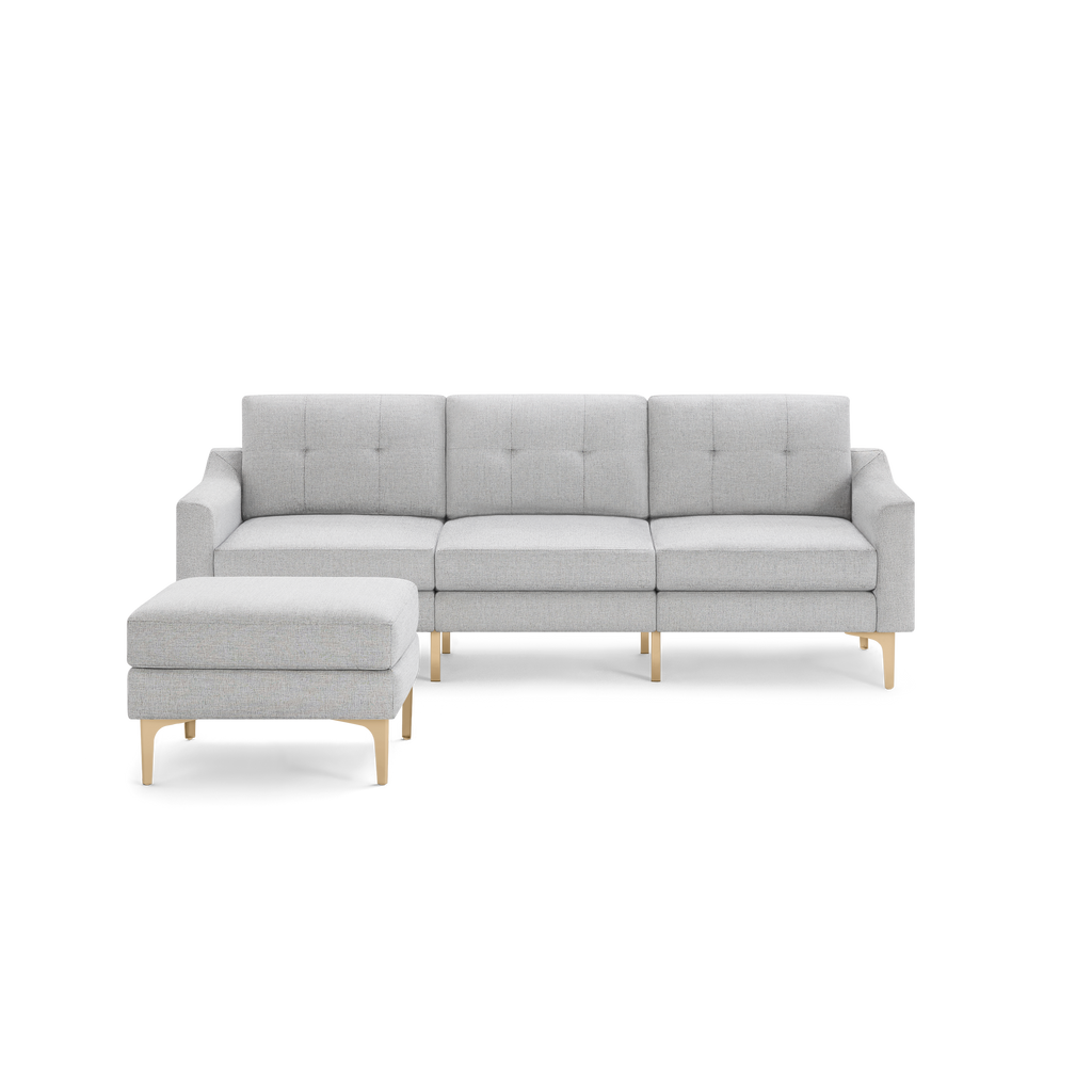 Light gray fabric sectional sofa with tufted back cushions and light wood legs, paired with a matching ottoman.