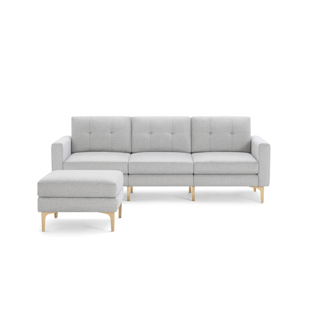 Light gray fabric sectional sofa with tufted cushions and light wood angled legs, paired with matching ottoman.