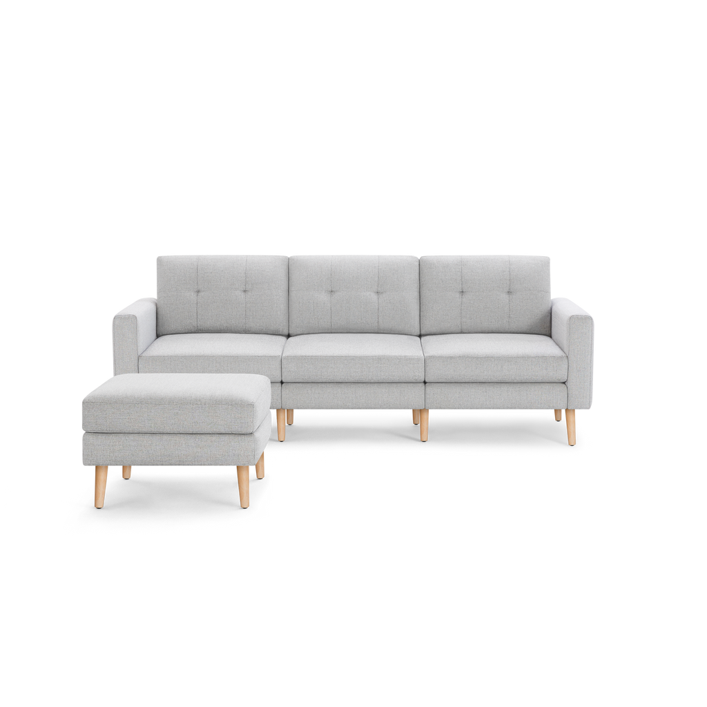 Light gray modern three-seater sofa with tufted backrests and matching ottoman, featuring wooden legs.