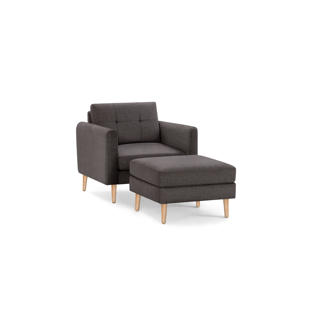 Dark gray fabric armchair with matching cushioned ottoman, both featuring wooden legs and modern, minimalist design.