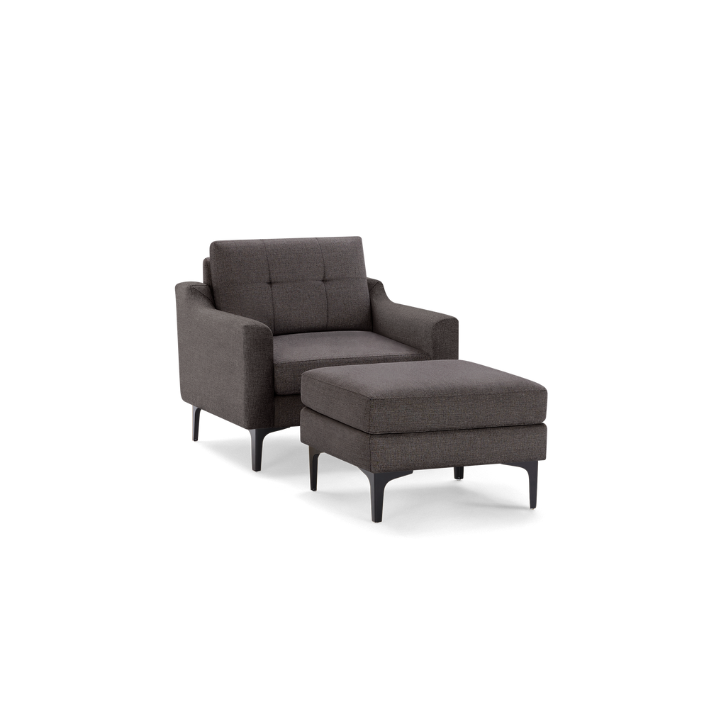 Dark gray upholstered armchair with tufted backrest and matching cushioned ottoman, both supported by black tapered legs.