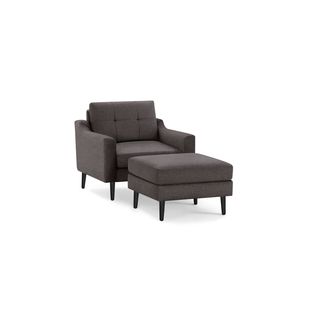 Dark gray upholstered armchair with matching cushioned ottoman, featuring black tapered legs and tufted backrest.