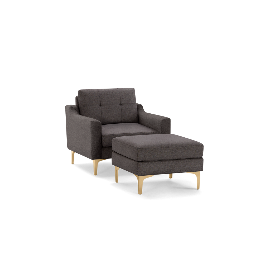 Dark gray upholstered armchair with matching ottoman, featuring tufted cushions and gold metal legs, modern design.